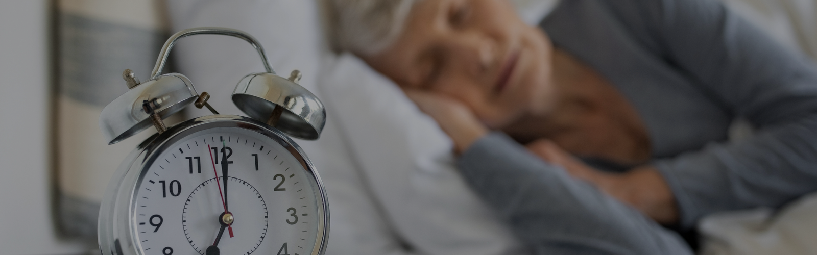 old person sleeping behind alarm clock