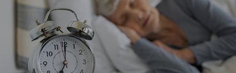 old person sleeping behind alarm clock